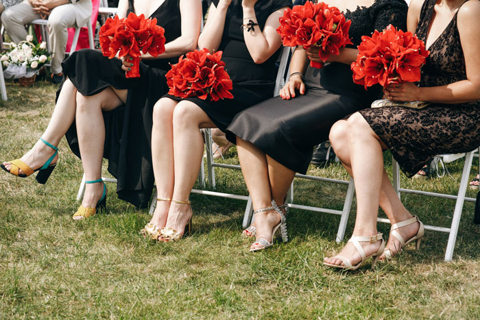 Bridesmaids in all-black dresses holding bold red bouquets at an outdoor wedding, highlighting dress code contrast. Bridesmaids in all-black dresses holding bold red bouquets at an outdoor wedding, highlighting dress code contrast.