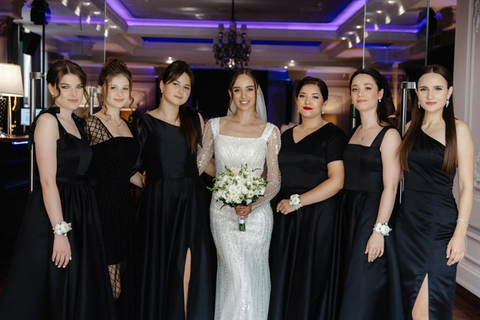 Bride in white dress with bridesmaids wearing all-black dresses at wedding, except one bold red dress breaking the dress code. Bride in white dress with bridesmaids wearing all-black dresses at wedding, except one bold red dress breaking the dress code.