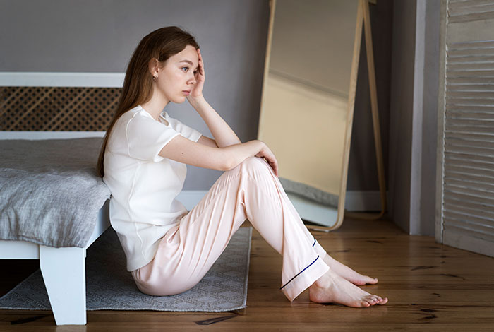 Young woman sitting on the floor looking worried, depicting bride’s family conflict after fiancé's legal threats. Young woman sitting on the floor looking worried, depicting bride’s family conflict after fiancé's legal threats.