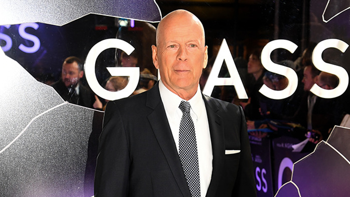 Bruce Willis at a public event, wearing a black suit and patterned tie, related to updates on his dementia.