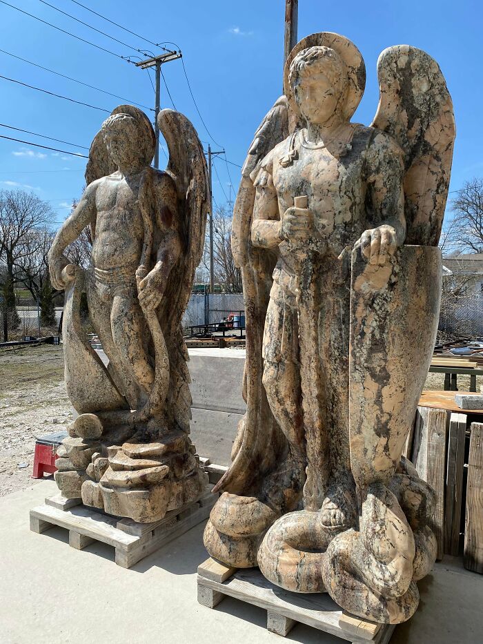 Two large marble statues of angels with shields and swords, showcasing creative people and their cool projects outdoors.