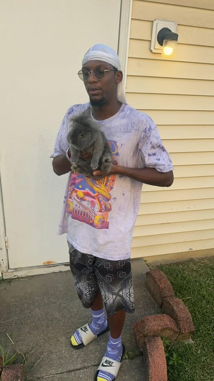 Man holding fluffy rabbit outside near house wall, showcasing funny and deceptive rabbit owner moments with playful pet fluffball.