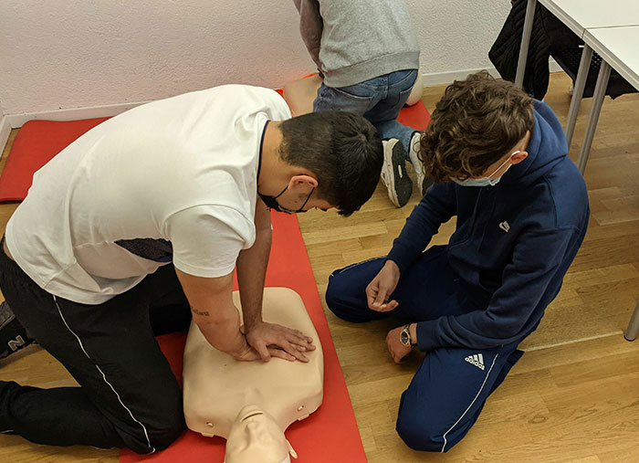Two young men practicing CPR on a training dummy, learning life-changing emergency response skills.