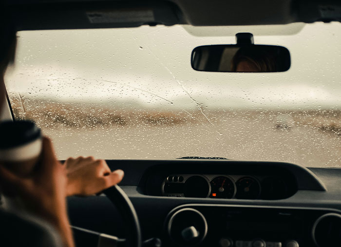 Person holding a coffee cup while driving through rain with water droplets on the windshield, symbolizing a bad day turning life-changing.