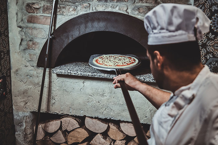 Chef baking a pizza in a stone oven, illustrating businesses that lost clients with poor decisions.