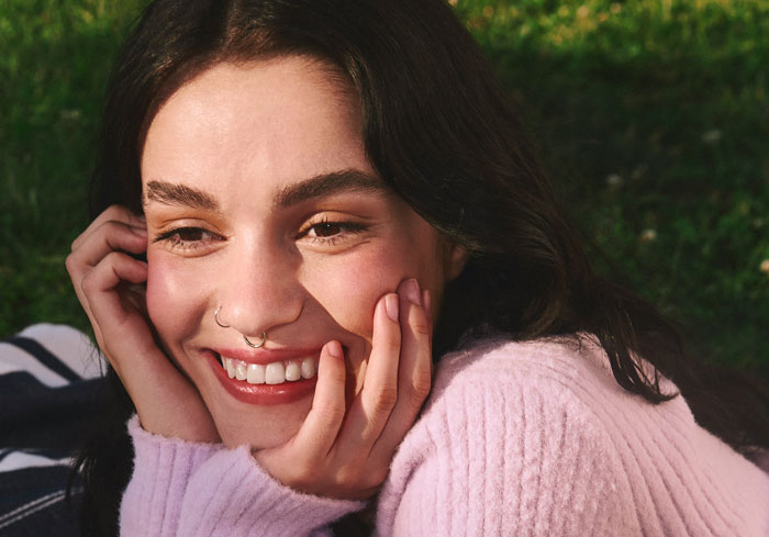 Young woman with a nose ring smiling outdoors, representing the lady who tells her grandkid she looks like a bull with her nose ring.