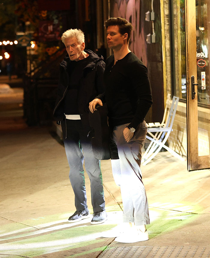 Calvin Klein, 83, standing outdoors at night with his boyfriend, 36, as they walk on a city sidewalk. Calvin Klein, 83, standing outdoors at night with his boyfriend, 36, as they walk on a city sidewalk.