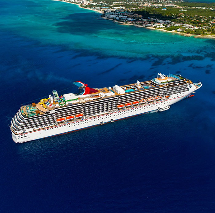 A large Carnival cruise ship sailing near a tropical coastline with clear blue water under bright sunlight. A large Carnival cruise ship sailing near a tropical coastline with clear blue water under bright sunlight.
