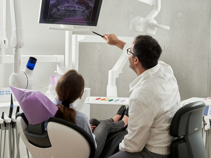 Dentist explaining dental X-ray to patient in modern clinic, reflecting wildest patient horror stories dentists recall.