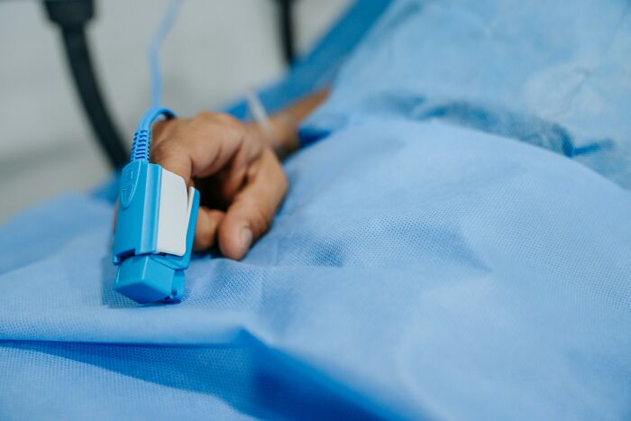 Patient wearing a blue medical gown with a pulse oximeter attached to their finger in a hospital setting