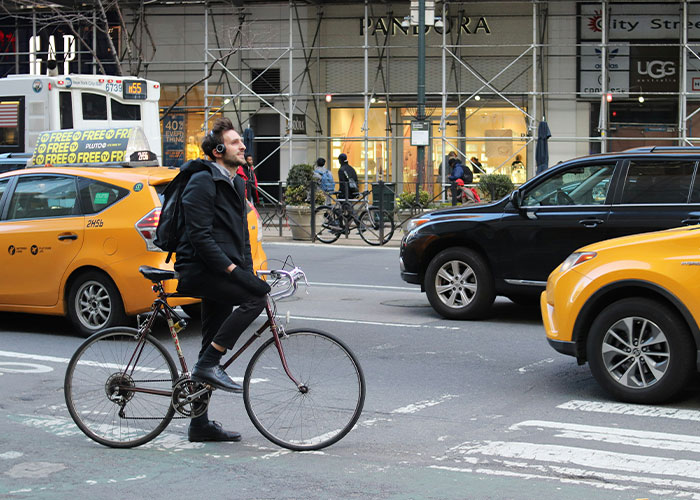 Man wearing headphones riding bicycle amid chaotic city traffic and yellow taxis on busy urban street.