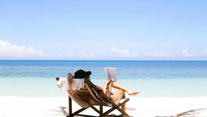 Person relaxing on a beach chair reading a book by the ocean, symbolizing uniquely awkward weddings that crashed and burned.
