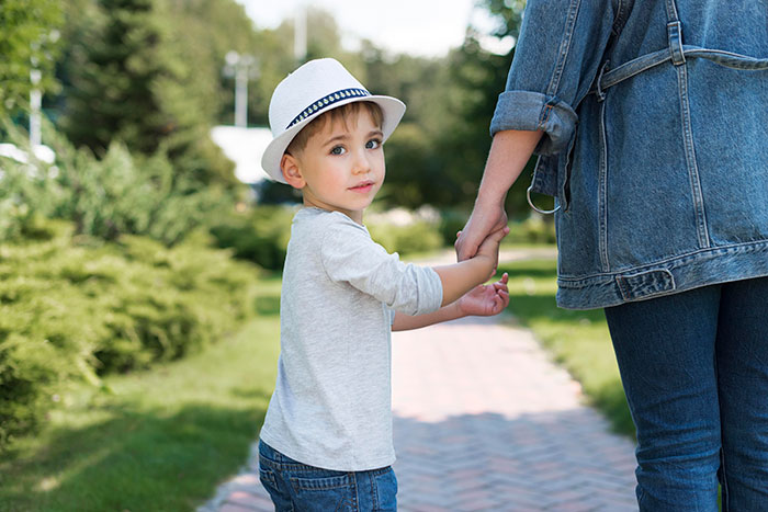 Young boy in a white hat holding an adult’s hand outdoors, reflecting blended family and in-laws Christmas tension.