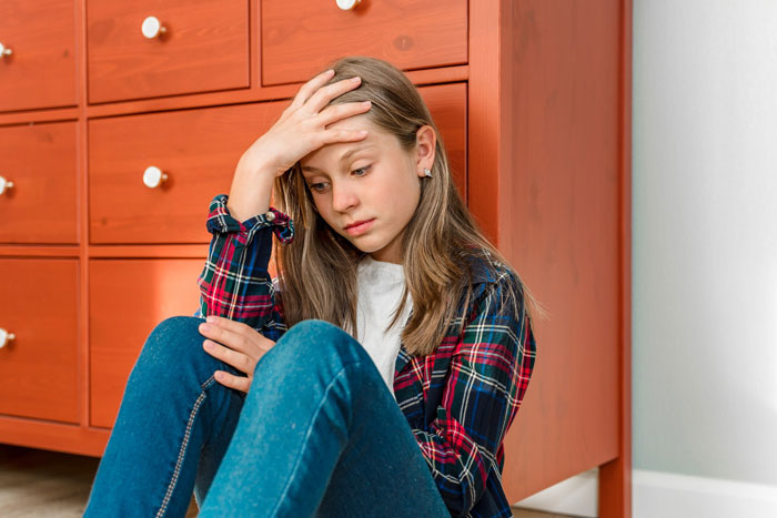 Teen girl looking stressed sitting on floor by dresser, highlighting irresponsible teen parenting and sibling CPS involvement. Teen girl looking stressed sitting on floor by dresser, highlighting irresponsible teen parenting and sibling CPS involvement.