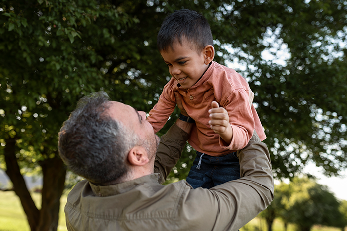 Man lifting young boy outdoors under trees, symbolizing family health fund dispute, woman suing half-brother over plastic surgeries. Man lifting young boy outdoors under trees, symbolizing family health fund dispute, woman suing half-brother over plastic surgeries.