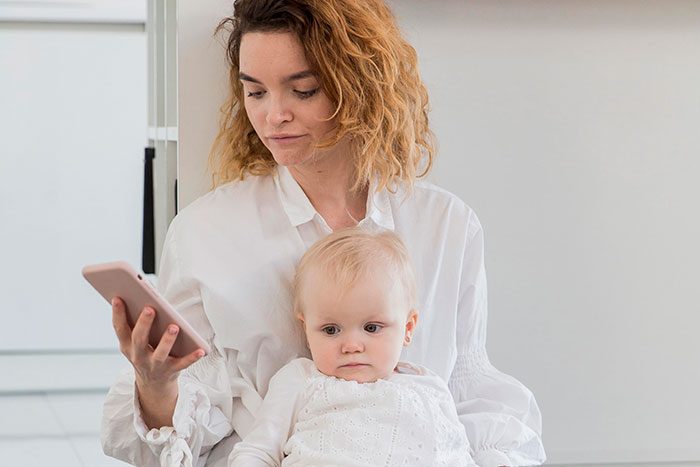 Woman on phone holding baby, appearing concerned during family vacation involving childfree cousin and kids. Woman on phone holding baby, appearing concerned during family vacation involving childfree cousin and kids.