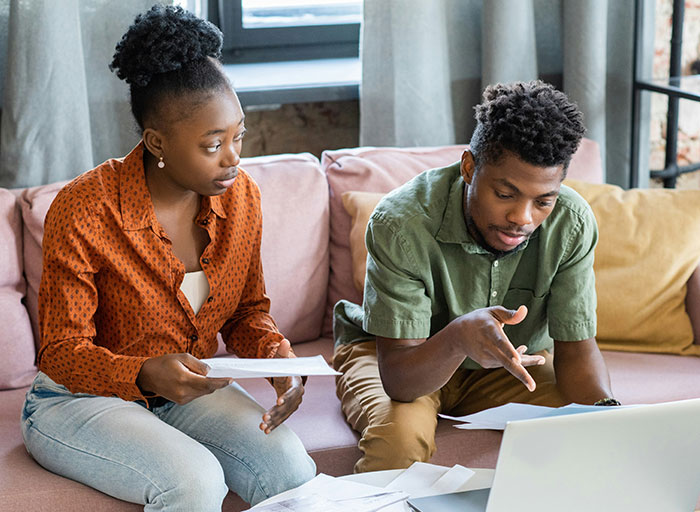 Couple discussing finances while seated on couch, reflecting on choosing nose job over kids college funds decision. Couple discussing finances while seated on couch, reflecting on choosing nose job over kids college funds decision.