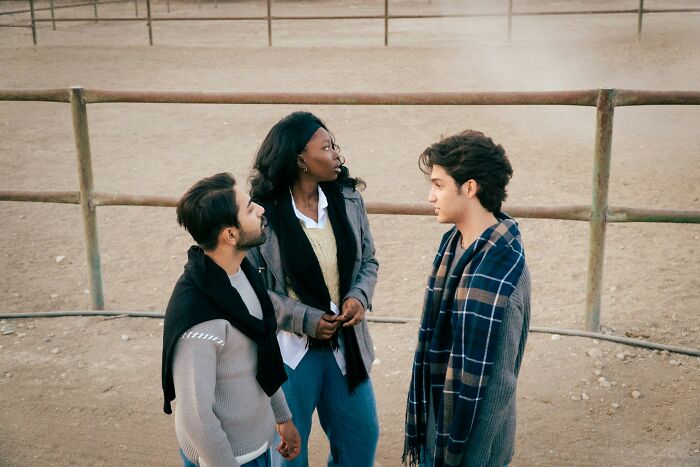 Three young adults in casual clothes having a serious conversation outdoors reflecting love and friendship issues.