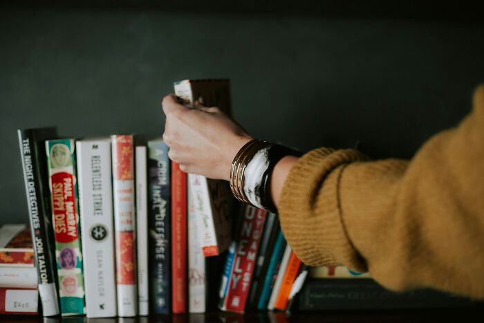 Person wearing bracelets picking a book from a shelf, symbolizing subtle signs that indicate cheating behaviors.