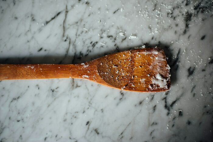 Wooden cooking spoon with flour dust on a marble surface, illustrating the etymology of common words in kitchens.
