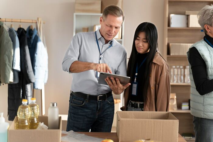 Man and woman in work lanyards discussing shipping details on a tablet in a warehouse setting at work.