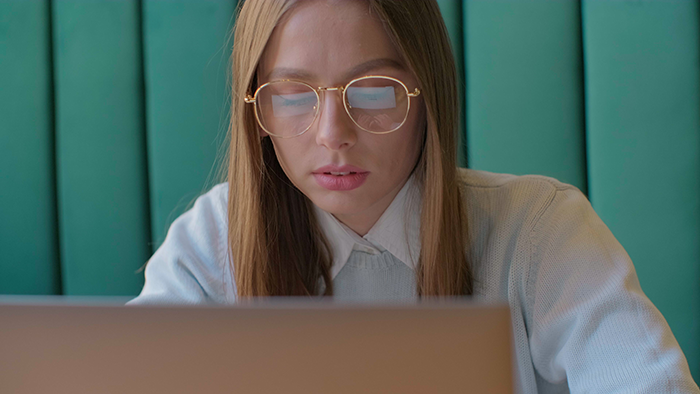 Woman with glasses looking at laptop screen, focused and concerned, exposing cheaters in an online investigation. Woman with glasses looking at laptop screen, focused and concerned, exposing cheaters in an online investigation.