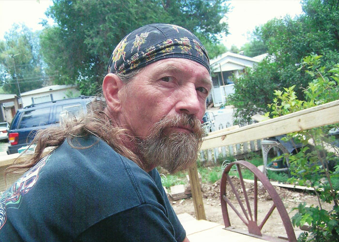 Middle-aged man with beard and bandana sitting outside near a wooden railing, related to missing woman’s body discovery case.