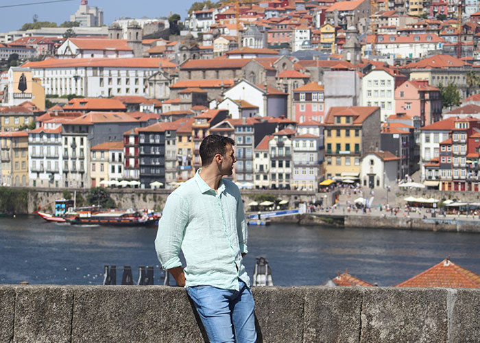 Man in casual clothes overlooking colorful European riverside buildings, illustrating life better in Europe versus USA debate