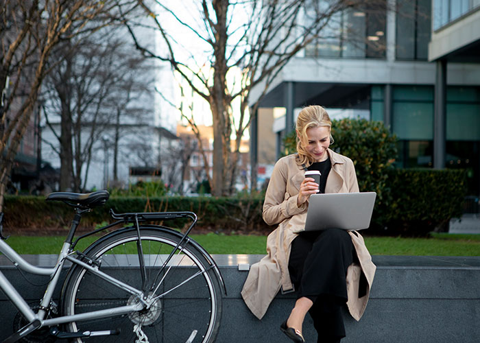 Woman sitting outdoors with laptop and coffee, reflecting on life in the USA and Europe debate.