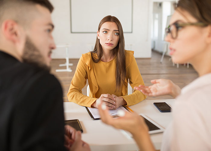 Three young adults engaged in a serious discussion, debating life quality in the USA versus Europe around a table.