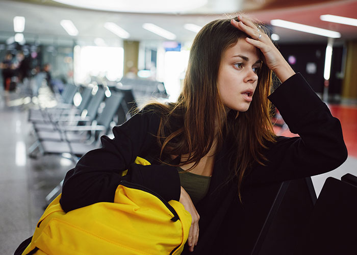 Young woman looking thoughtful in an airport lounge, reflecting on life in the USA versus Europe debate.