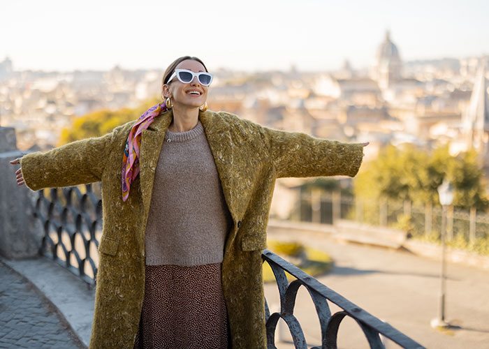 Woman enjoying a sunny day overlooking a European city, reflecting on whether life is better in the USA or Europe.