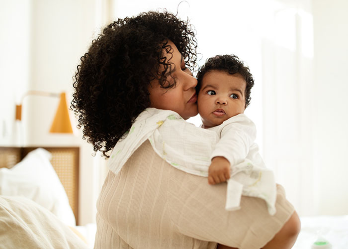 Mother holding and kissing her baby, illustrating the debate on whether life is better in the USA or Europe.