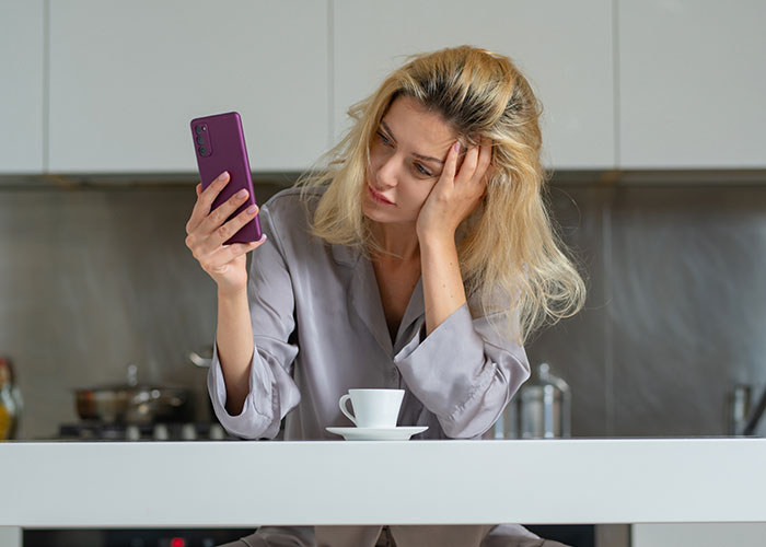A woman looking thoughtfully at her phone, reflecting on life in the USA or Europe debate over coffee.