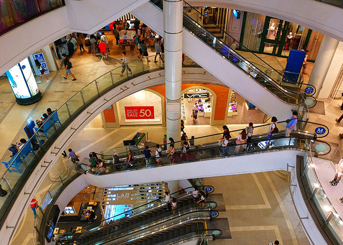 Shoppers on multiple escalators inside a busy mall, illustrating daily life and lifestyle differences in the USA and Europe.
