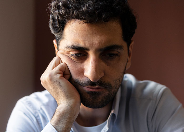 Man with curly hair resting his face on hand, deep in thought about life in the USA versus Europe debate.