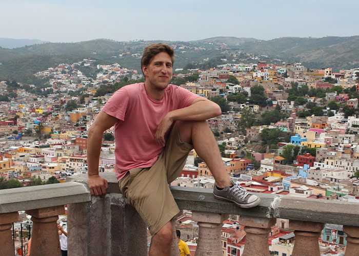 Young man in casual clothes overlooking a colorful European city, reflecting on life in the USA versus Europe debate.