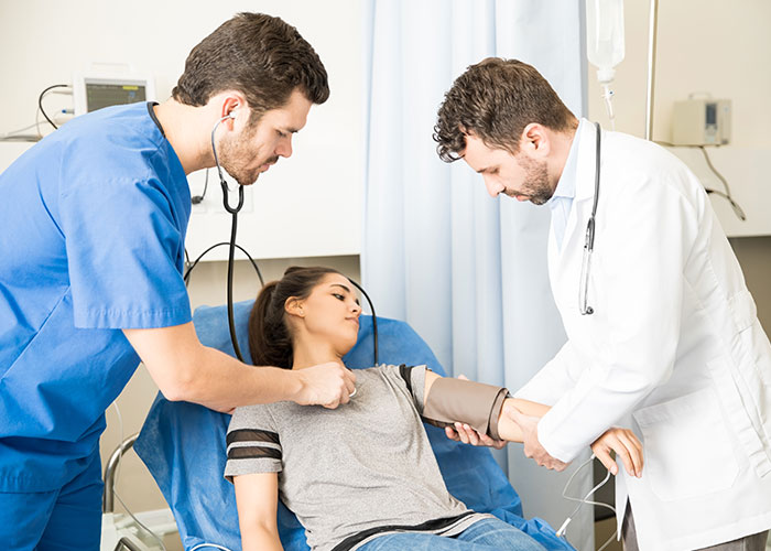 Two doctors check a young woman’s blood pressure in a clinic, illustrating life and healthcare standards in the USA or Europe.