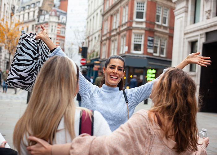 Three happy women reunited outdoors in a city setting, reflecting life and social moments in the USA and Europe debate.