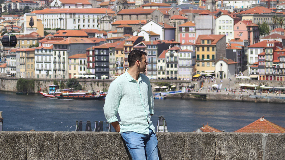 Man in a light shirt overlooking colorful European riverside buildings, reflecting life better in Europe or USA debate.