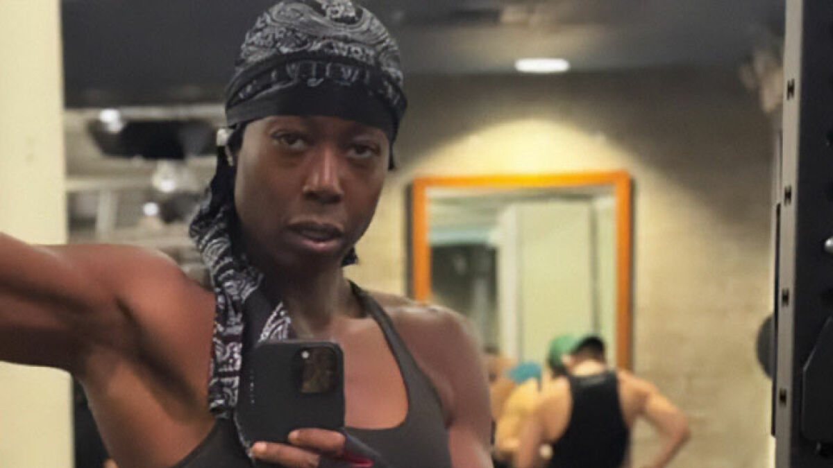 Person wearing a bandana and tank top taking a gym mirror selfie amid uproar over lesbian confronting alleged trans woman.