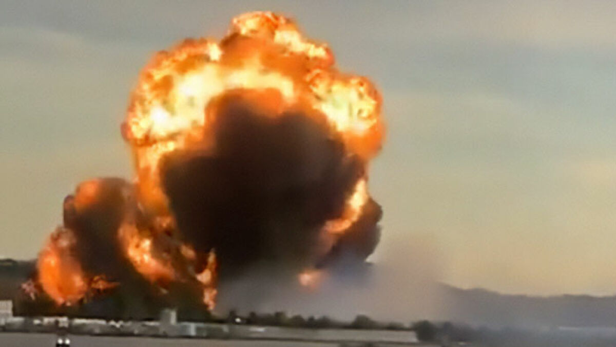 Massive fiery explosion from UPS plane crash with thick black smoke rising over a distant landscape at sunset.