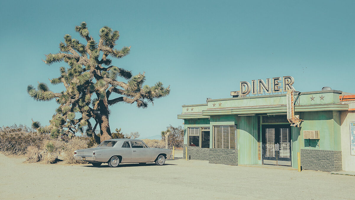 Vintage car parked near a rustic diner with a Joshua tree in the background under a clear blue sky in the Wild West.