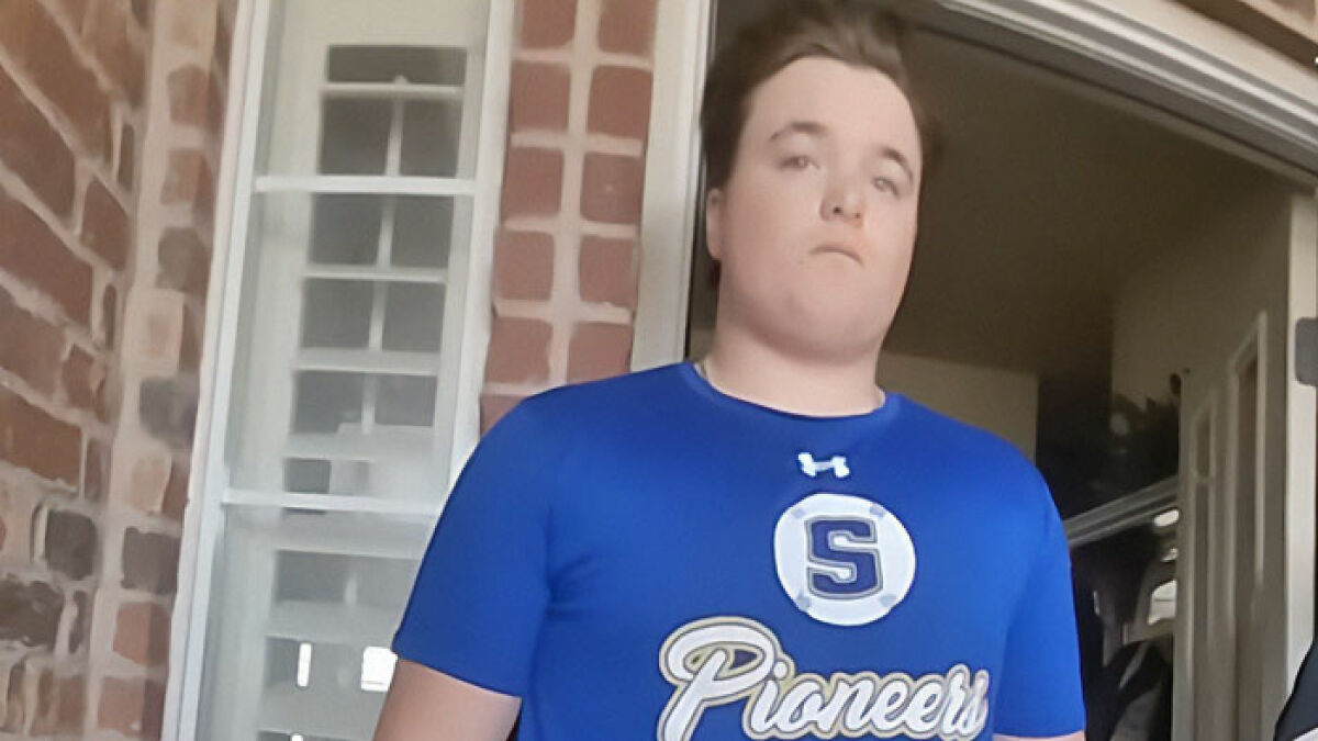Teen wearing blue Pioneers shirt standing near brick wall amid Oklahoma protests over controversial case.