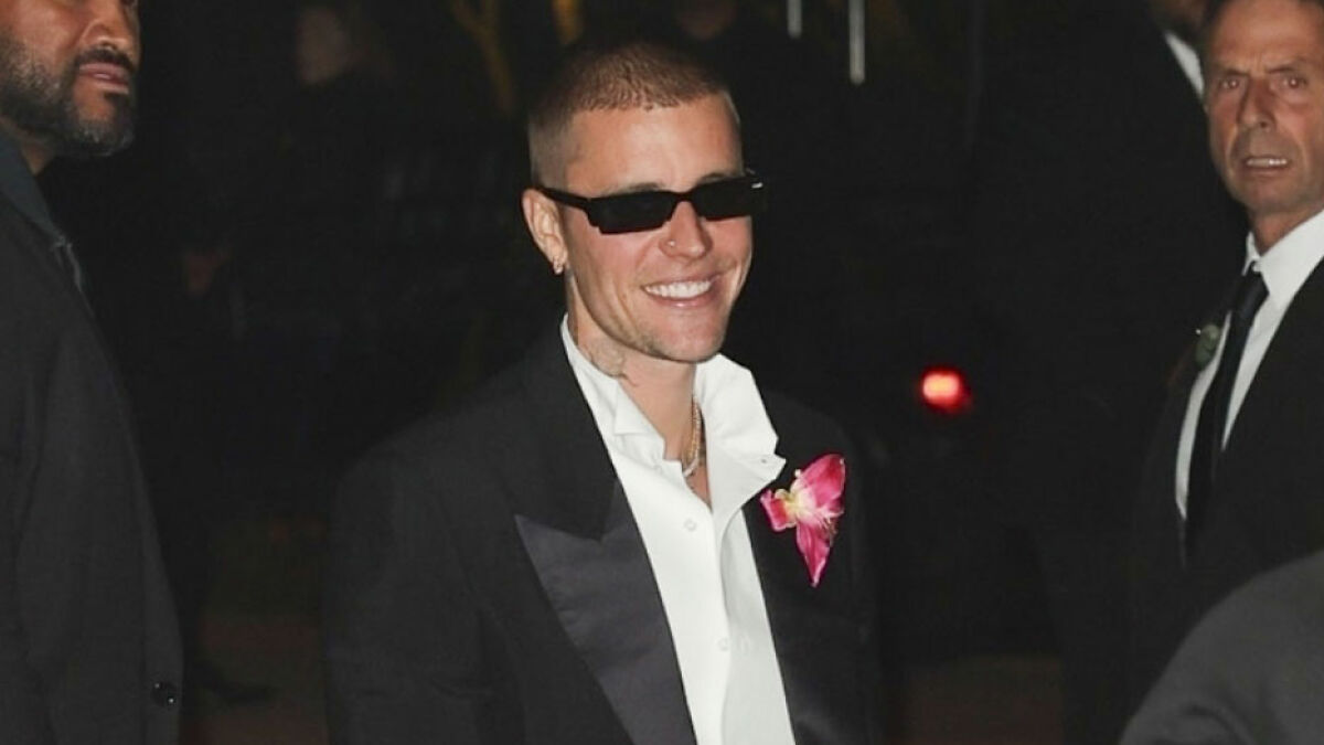 Justin Bieber smiling in a black tuxedo with sunglasses, fans expressing concern after noticing something on his c****h.