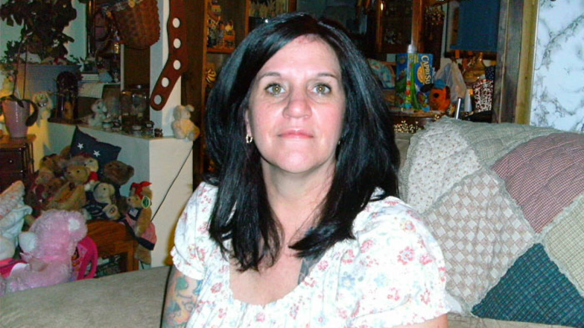 Woman with dark hair sitting on a couch surrounded by stuffed animals and household items missing womanu2019s body keywords.
