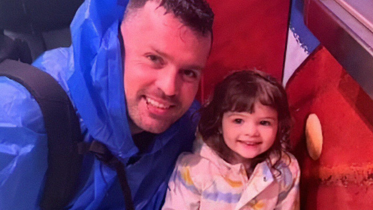 Man in blue jacket smiling with young child, related to dad who left 2YO in car during adult video binge story.