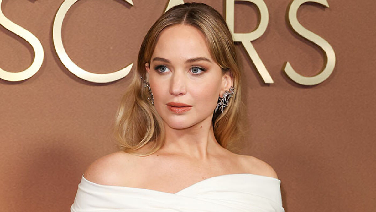 Jennifer Lawrence in a white off-shoulder dress posing at an event amid plastic surgery speculation and dress controversy.