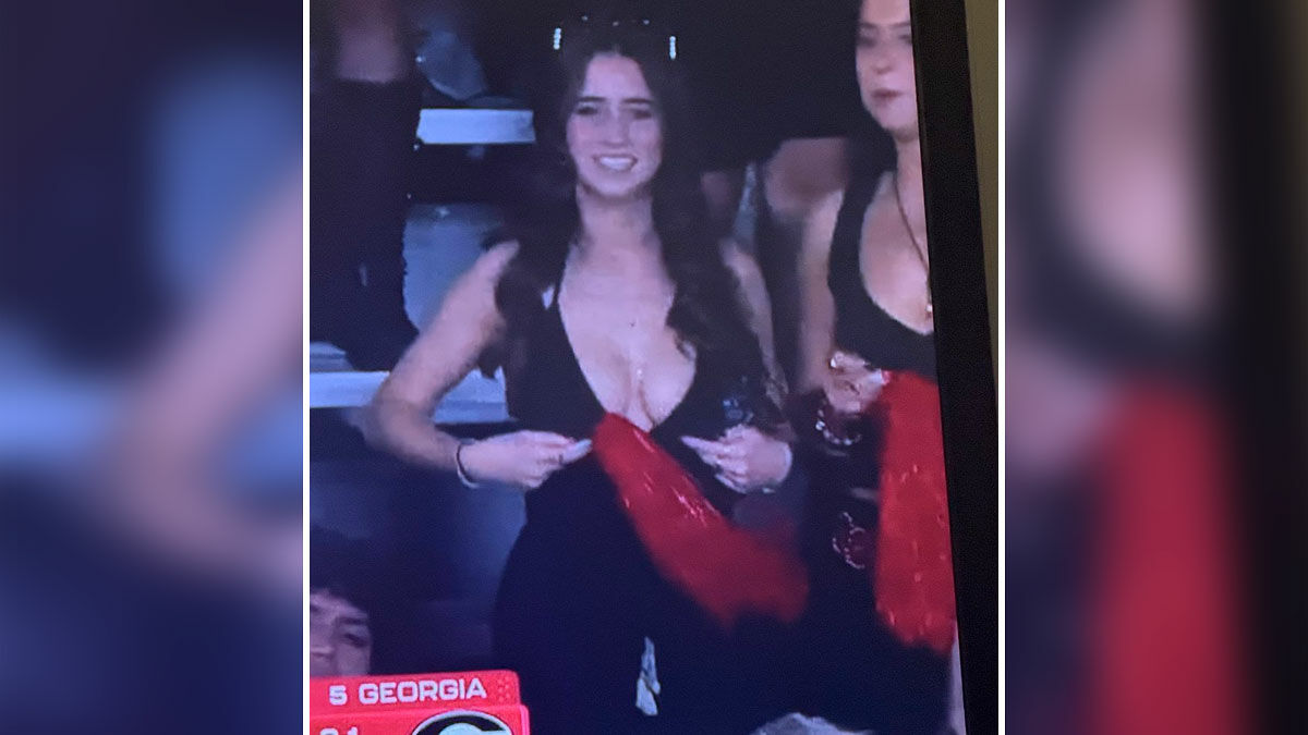 Young stunning woman wearing black dress smiling and holding red scarf at Georgia-Texas game crowd.