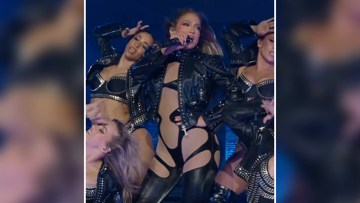 Jennifer Lopez performing a risquu00e9 dance wearing black cutout outfit and leather jacket with backup dancers on stage.
